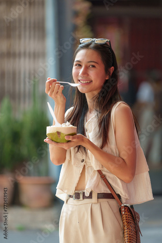 Photography A beautiful Asian woman wearing casual clothes and glasses with a headband is eating delicious fruit in a street food market in the evening