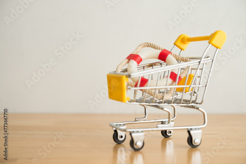 Lifebuoy in shopping trolley on wooden table with white wall background. Purchase life, health, travel or others insurance online internet and offline concept. Easy to buy the best deal insurance.