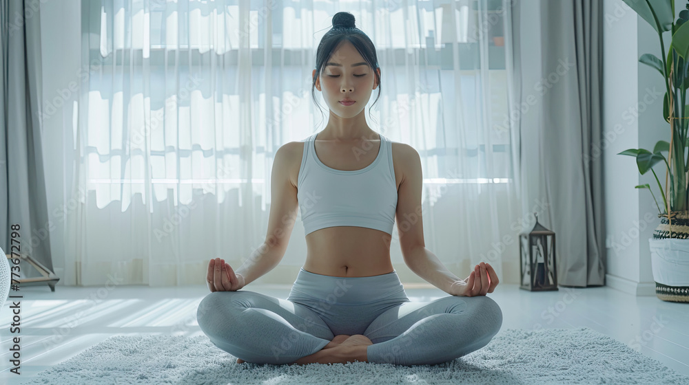 Calm of wellness Asian young woman sit on carpet breathing with yoga lotus pose Yoga meditation of young healthy woman relax and comfortable at white cozy home Yoga Exercise for Wellness Concept.