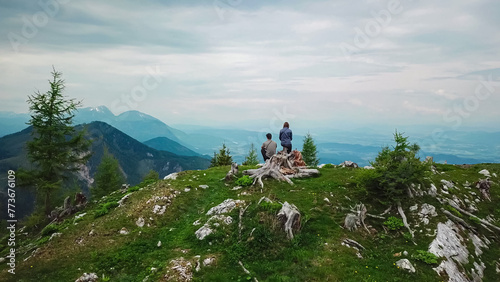 Hiker couple on alpine meadow near Feistritzer Spitze (Hochpetzen) with panoramic view of majestic mountain peaks Karawanks and Julian Alps, Carinthia, border Austria Slovenia. Hiking trail Petzen photo
