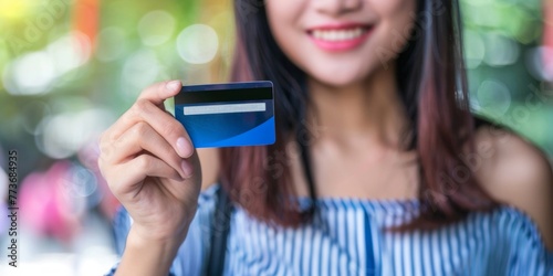 A woman standing outdoors holding a credit card in her hand, smiling