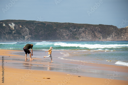 child with dad playing on the beach by the sea