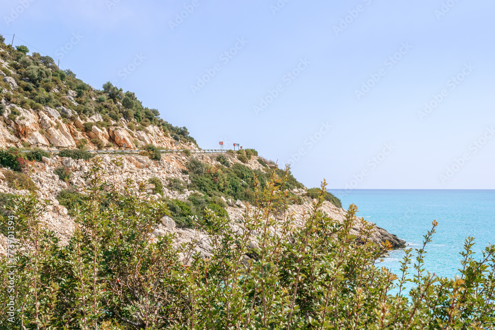 A picturesque rocky beach in the Mediterranean Sea with clear blue water and stones. Road on a cliff near to sea. Demre, Turkey.