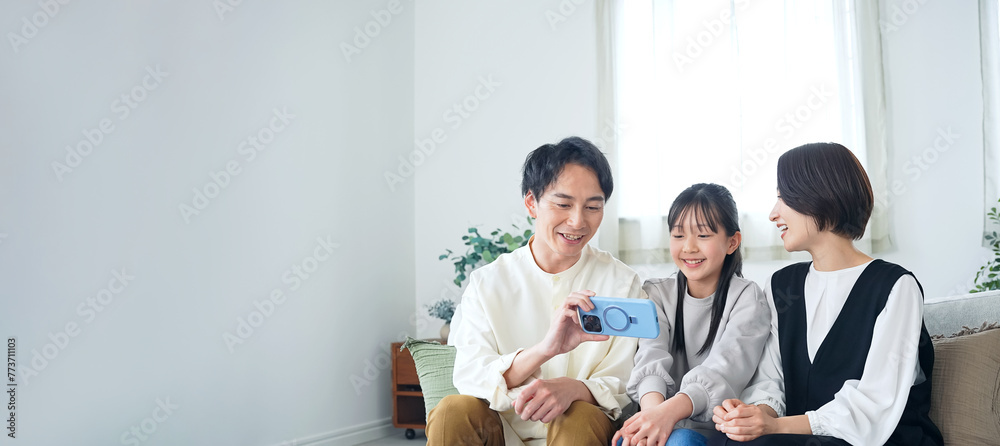 A family of an Asian girl and her parents looking at a smartphone screen. A family of an Asian girl and her parents looking at a smartphone screen.