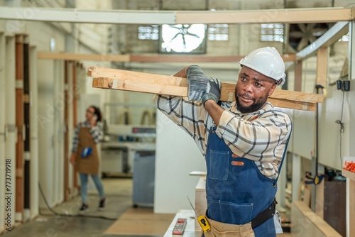 Carpenter man Portrait of Young black skin working in workshop. Happy professional Carpenter holds wooden planks for build furniture in carpentry workshop. carpenter worker make furniture in DIY shop
