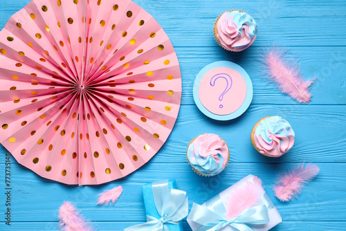 Delicious cupcakes with question mark, gift boxes and decorations on blue wooden background. Gender reveal party concept photo