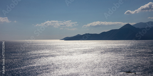 Silver water against blue cloudy sky background. Mountain silhouette, sparkle ripple sea. Wallpaper