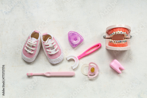 Children's toothbrushes with pacifier, jaw model and shoes on white grunge background