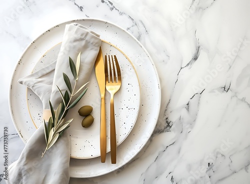 Photo of golden cutlery on a white plate with a napkin and olive branch, in a top view, flat lay isolated on a marble table background, mockup for a menu or restaurant ad