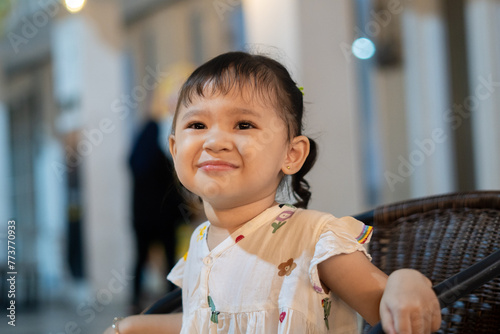 Cute lil' girl sitting on wooden chair and smiling photo