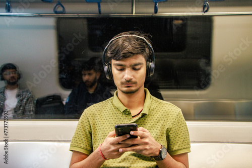 Portrait of young Indian man passenger traveling and using his smartphone in the metro or subway train. Metro and Public transportation concept. Bengaluru, India.