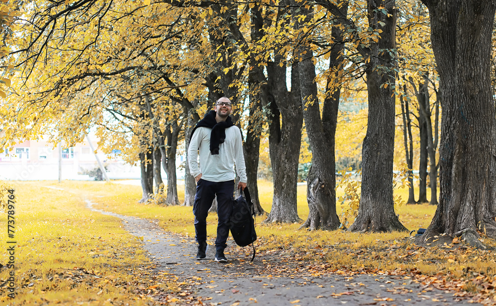Fototapeta premium A young man in glasses walks in the park with an umbrella during the rain.