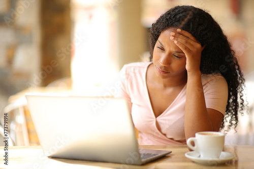 Worried black woman checking laptop content in a bar