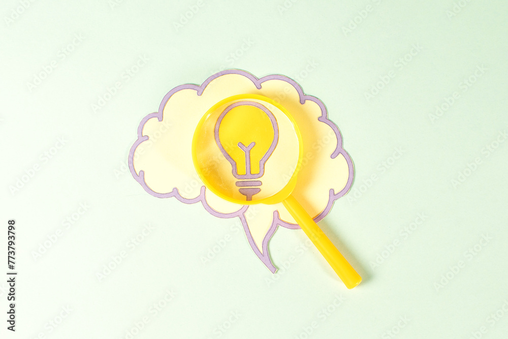 A yellow light bulb is magnified by a yellow magnifying glass on brain,