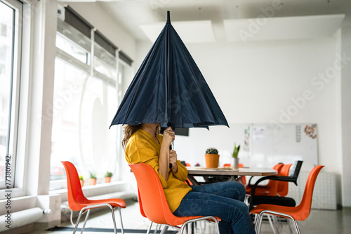 Creative businesswoman holding folded umbrella covering face at workplace photo