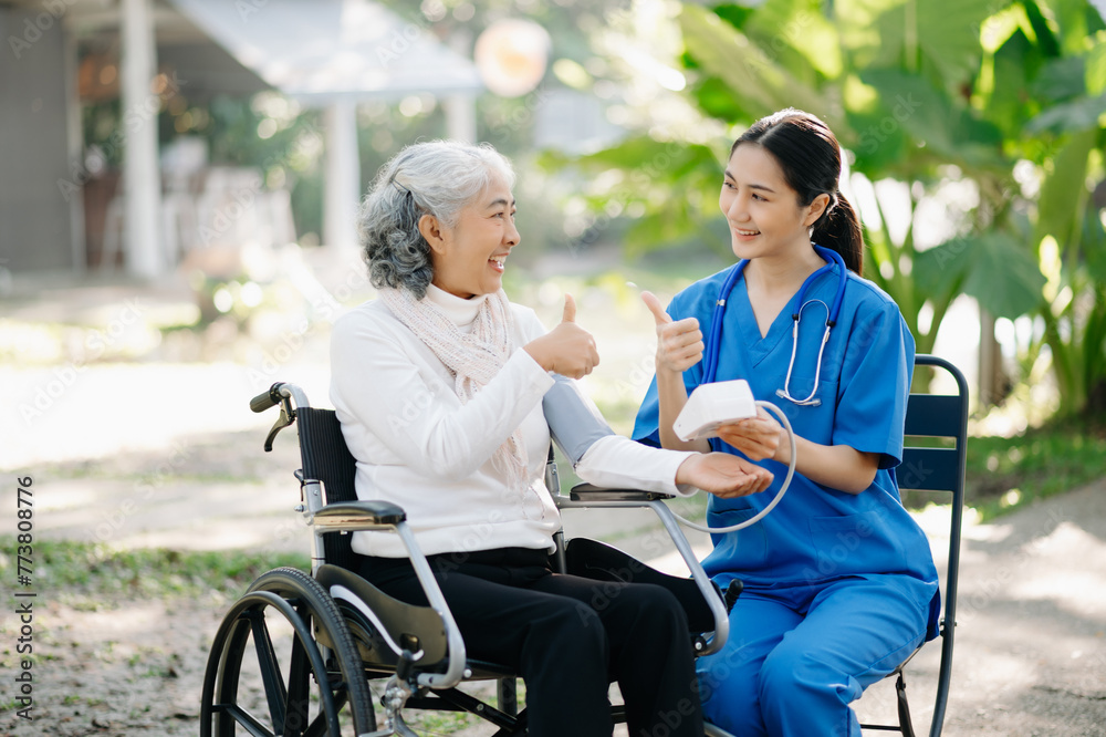 Elderly asian senior woman on wheelchair with Asian careful caregiver and encourage patient, walking in garden. with care from a caregiver Elderly asian senior woman on wheelchair with Asian careful caregiver and encourage patient, walking in garden. with care from a caregiver