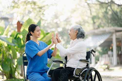 Elderly asian senior woman on wheelchair with Asian careful caregiver and encourage patient, walking in garden. with care from a caregiver