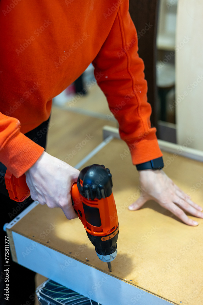 carpenClose up of a woman using cordless screwdriver for assembling furniture at home. Independent woman repairing furniture at home.ter working on a saw