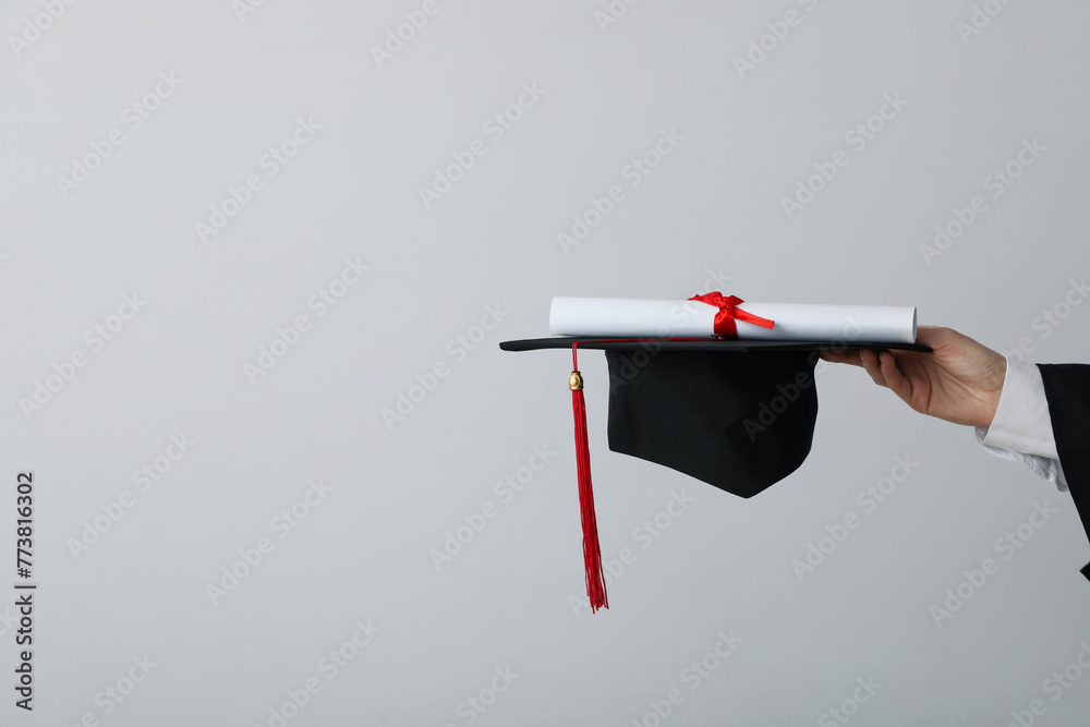 Naklejka premium Diploma and hat of a university graduate, on a gray background.