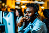 A cheerful African man wearing a headset and working at a computer in a bustling office environment