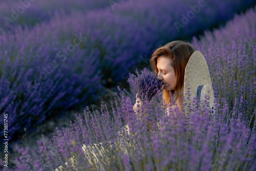 Fototapeta Naklejka Na Ścianę i Meble -  Woman poses in lavender field at sunset. Happy woman in yellow dress holds lavender bouquet. Aromatherapy concept, lavender oil, photo session in lavender