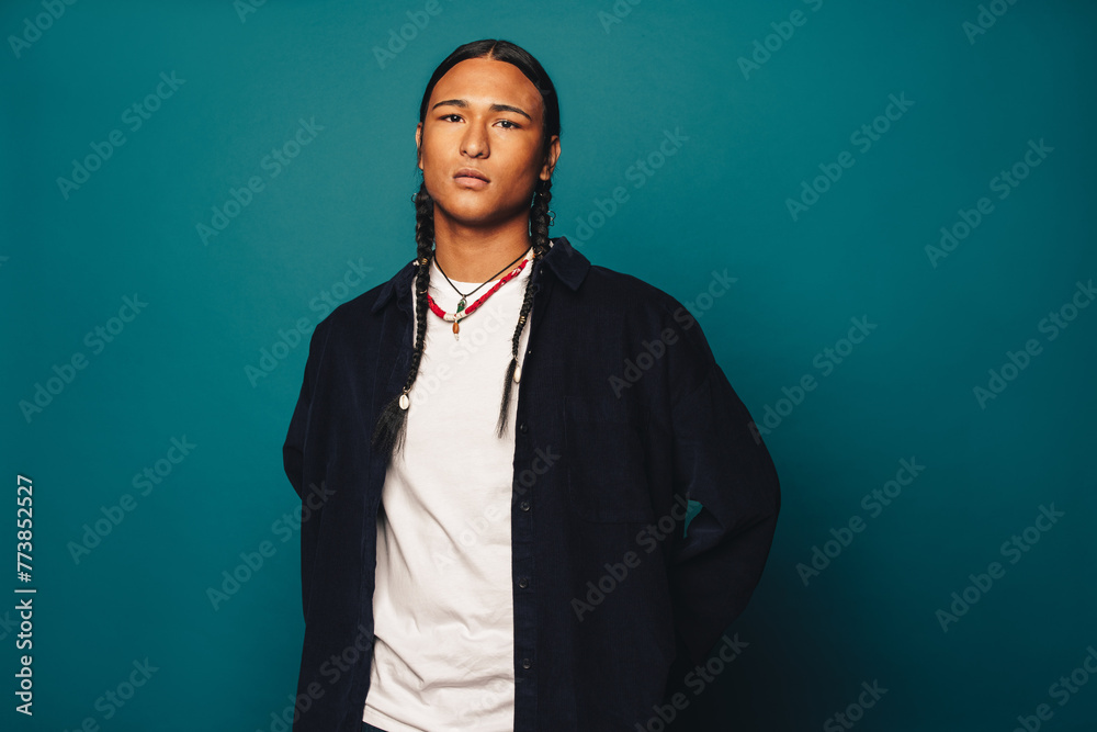Confident native american man with stylish braided hair and jewelry standing on blue background - obrazy, fototapety, plakaty 