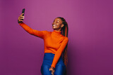 Smiling african woman taking a selfie with smartphone on a vibrant purple background