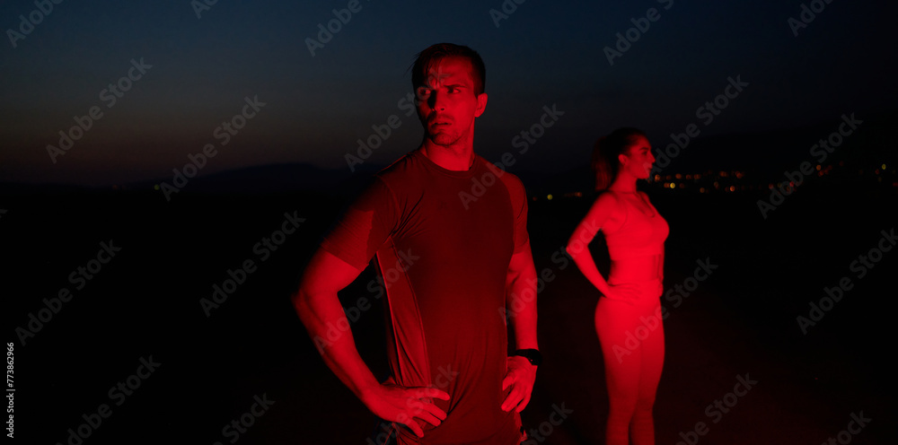 Athlete Strikes a Pose Under Red Nighttime Glow After Intense Daylong Marathon. - obrazy, fototapety, plakaty 