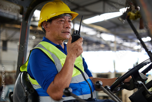 senior worker using walkie talkie and holding steering wheel on forklift truck in the factory photo
