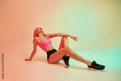 Sitting on the floor. Sportive woman with pink wig is against background