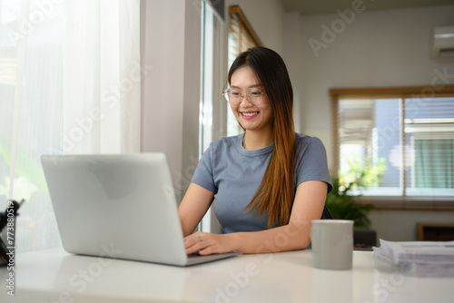 Attractive young woman working remotely at home, using laptop on table in living room © Prathankarnpap