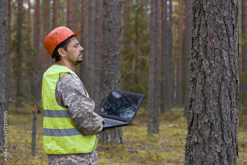 Forest engineer works in the forest with a computer. Trees are reflected on the computer screen.