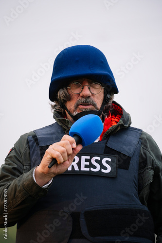 Press reporter in bulletproof vest holding a microphone.