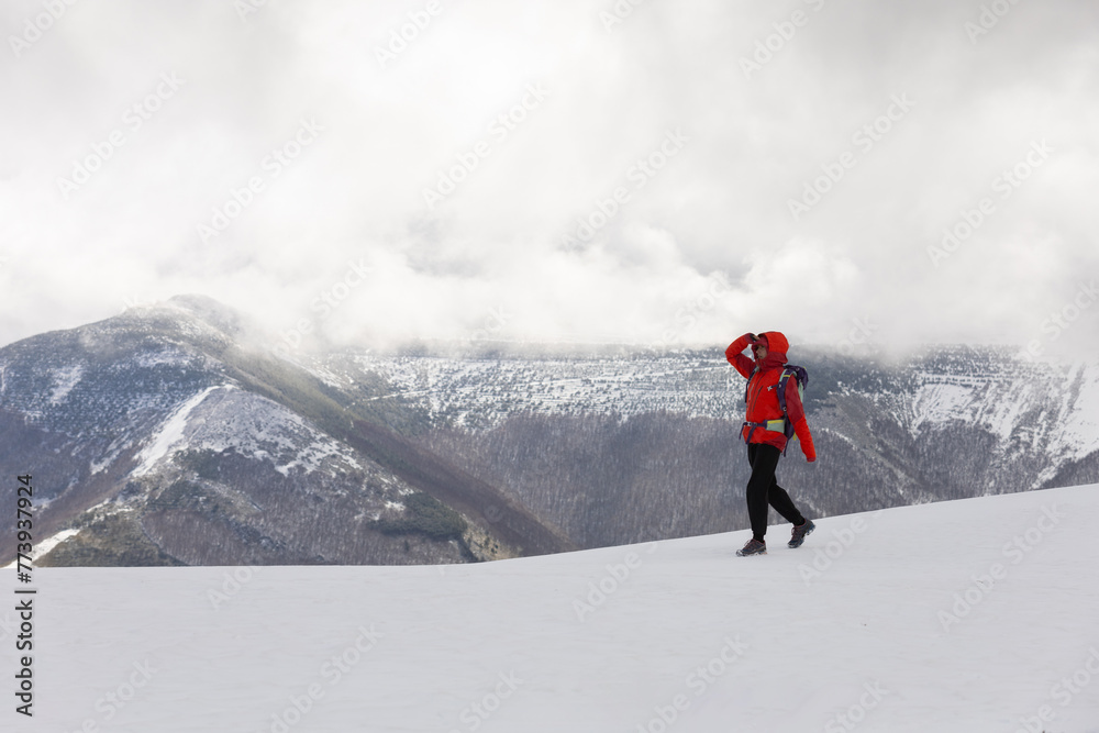A person in a red jacket is walking on a snowy mountain. The sky is cloudy and the mountain is covered in snow. The person is looking up A person in a red jacket is walking on a snowy mountain. The sky is cloudy and the mountain is covered in snow. The person is looking up