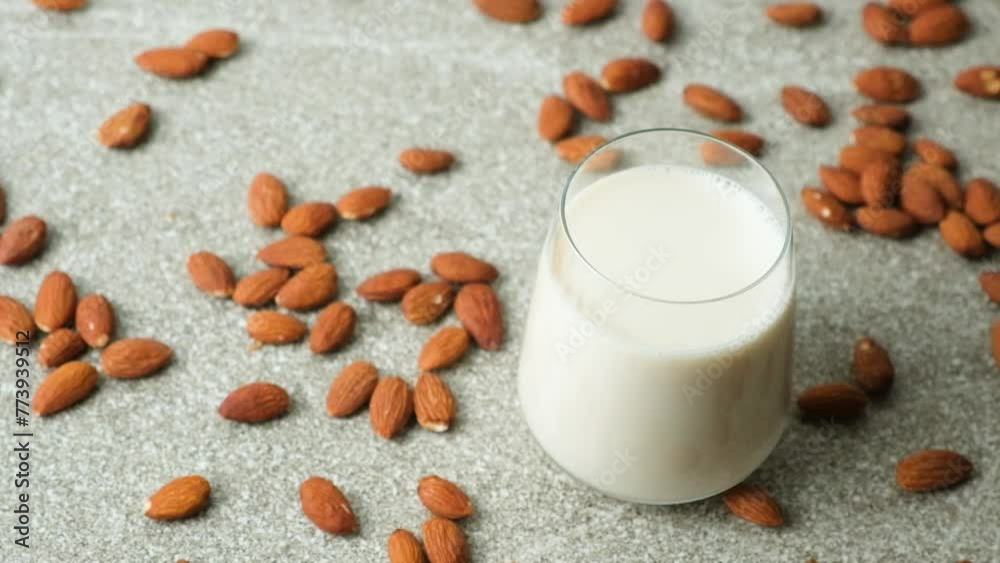 Almond milk in glass among scattered almonds on grey concrete background. Almond milk in glass among scattered almonds on grey concrete background.