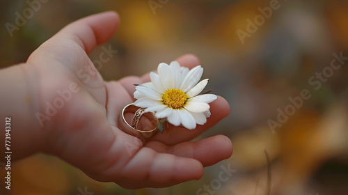A childs hand holding a flower next to a wedding invitation and ring. generative ai 