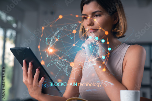 Smiling businesswoman in casual wear holding tablet device touching it at office workplace. Concept of distant work, business education, information technology.Blockchain hologram