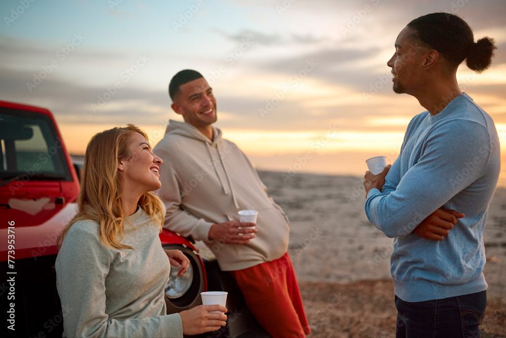 Group Of Friends Standing Chatting By Car With Hot Drink At Beach Watching Sunrise Together Group Of Friends Standing Chatting By Car With Hot Drink At Beach Watching Sunrise Together