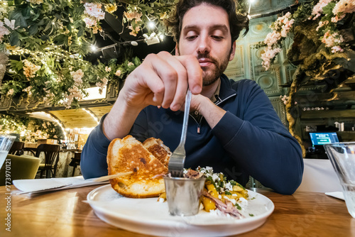 A man is engaged in enjoying a gourmet sandwich at a cafe, embellished with hanging garden decorations, offering a feast for the senses photo