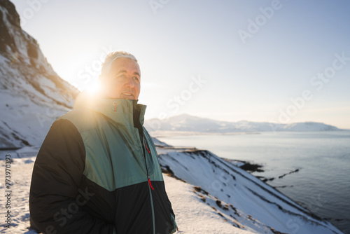 A traveler in a warm coat savors the tranquil moments of a sunlit winter day, overlooking the snowy coastline of Iceland photo