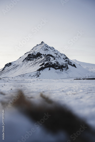 A solitary mountain rises sharply against the soft winter sky, its slopes dusted with fresh snow, embodying the silent beauty of Iceland photo