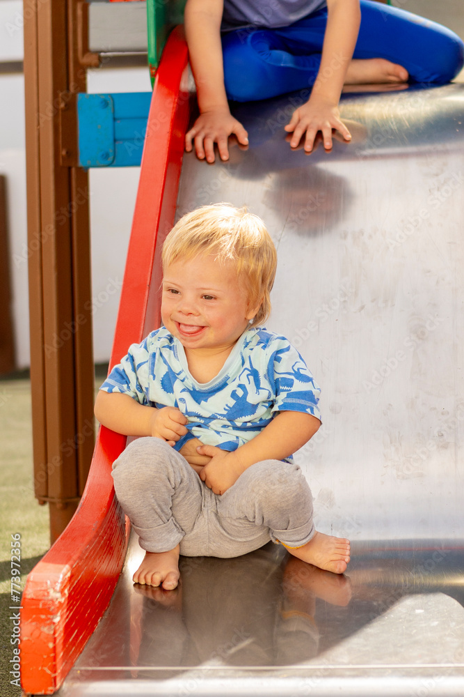 Happy toddler with Down syndrome enjoying playground slide Happy toddler with Down syndrome enjoying playground slide
