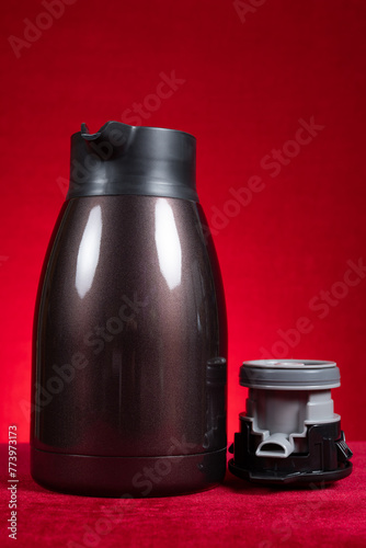 a stainless steel thermos bottle with the lid opened on red at vertical composition © Freer