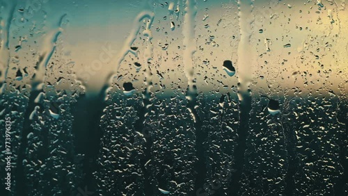 Evening rain plays a melancholic serenade on the glass, with droplets illuminated by a dusky glow photo
