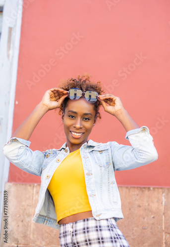 woman wearing a yellow shirt and blue jacket is smiling and holding sunglasses. Concept of happiness and carefree attitude