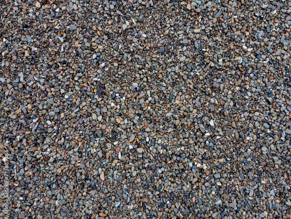 The texture of small variegated river stones. The background is made of small stones of different colors sifted from fine sand. The texture of small variegated river stones. The background is made of small stones of different colors sifted from fine sand.