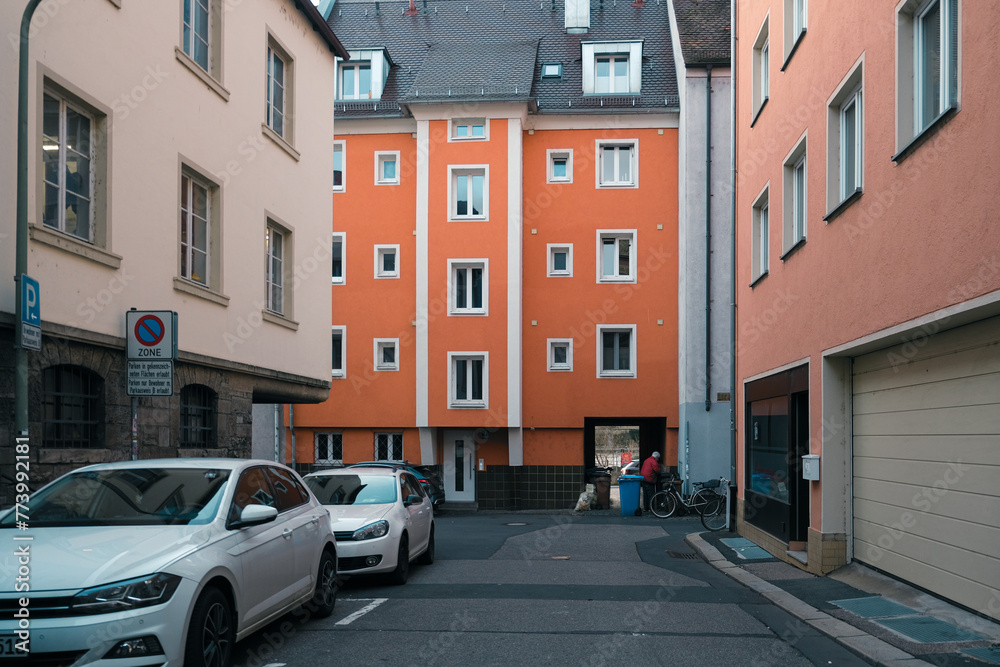 A white vehicle is parked in a tight alley between two orange buildings. Its automotive lighting shines on the narrow space A white vehicle is parked in a tight alley between two orange buildings. Its automotive lighting shines on the narrow space