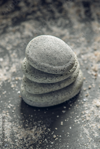 Natural soap in the shape of stones stacked on top of each other on a black background covered with sea salt. Concept of organic cosmetics and spa
