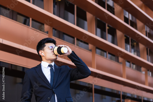 Young businessman with coffee standing outside office building