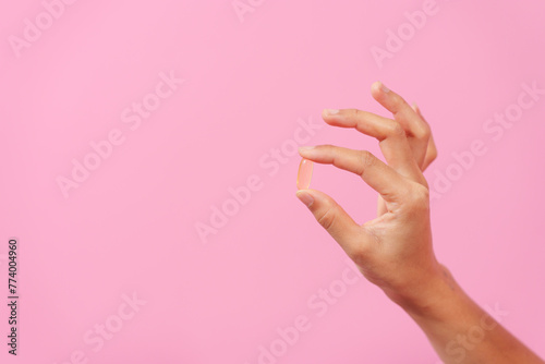 Gracefully, woman hand cradles a bottle of cod liver oil against a pink backdrop, representing health, nutrition, and the benefits of omega-3 supplementation.